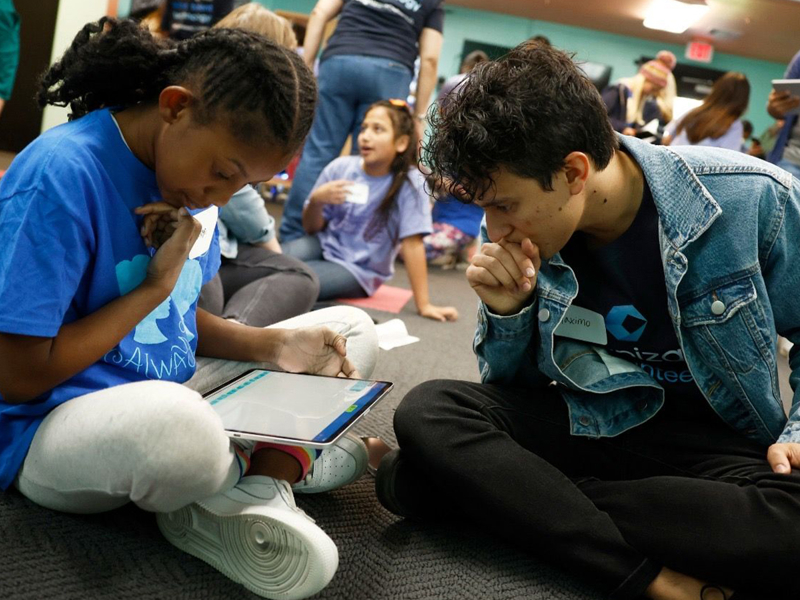 a person and person sitting on the floor looking at a tablet