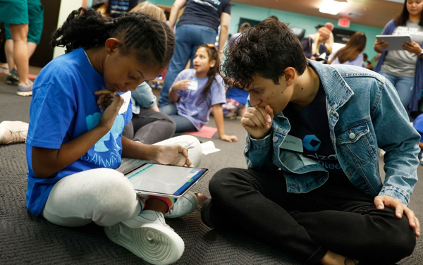 a person and person sitting on the floor looking at a tablet
