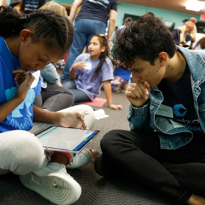 a person and person sitting on the floor looking at a tablet