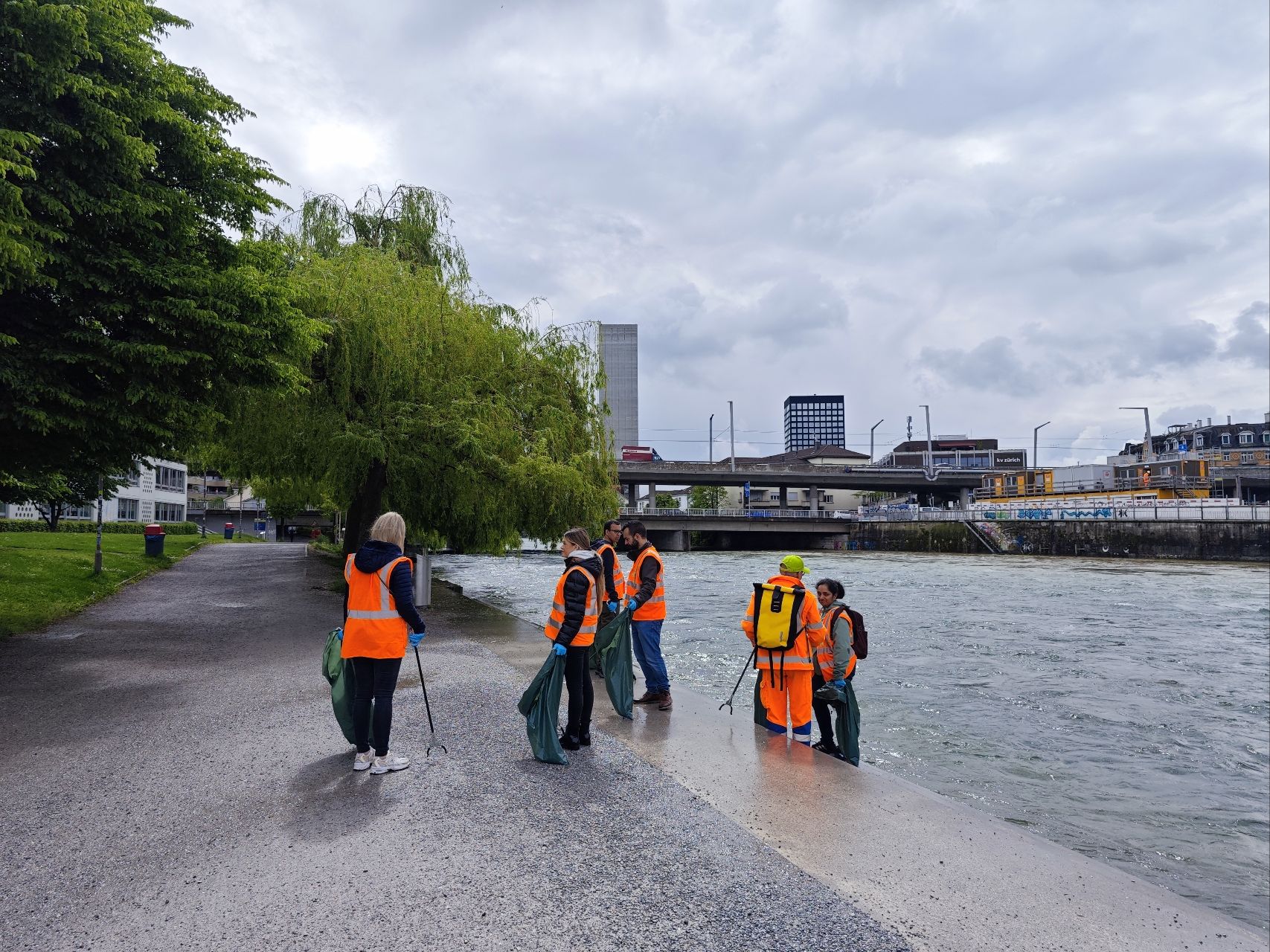 a group of people in orange vests standing on a sidewalk next to a body of water