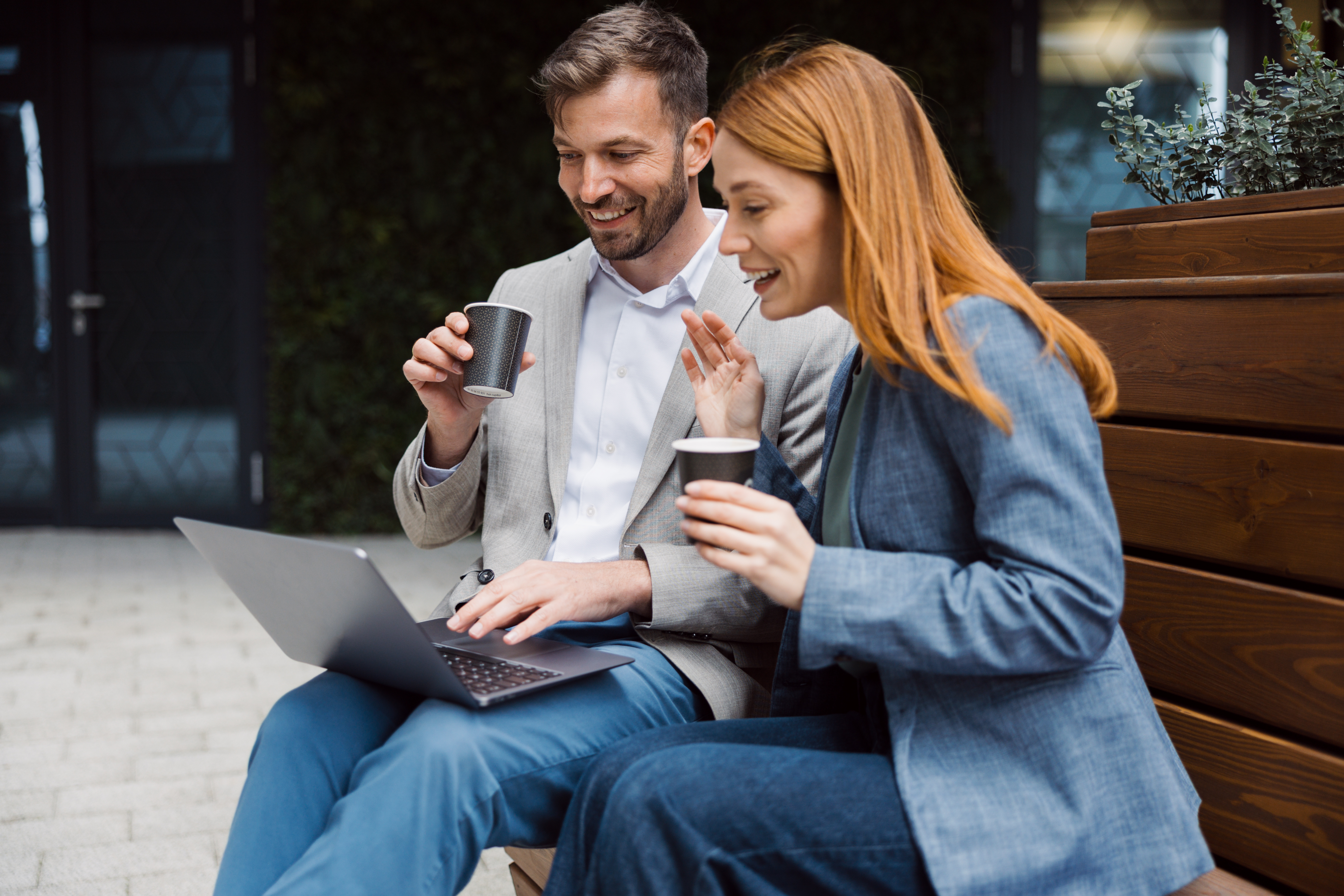 a person and person sitting on a bench with a laptop and coffee