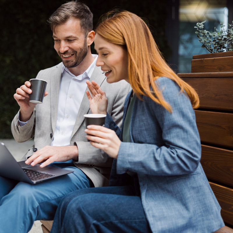a person and person sitting on a bench with a laptop and coffee