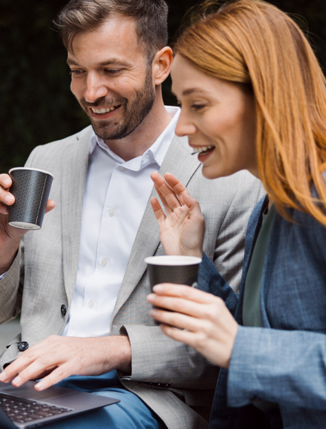 a person and person sitting on a bench with a laptop and coffee