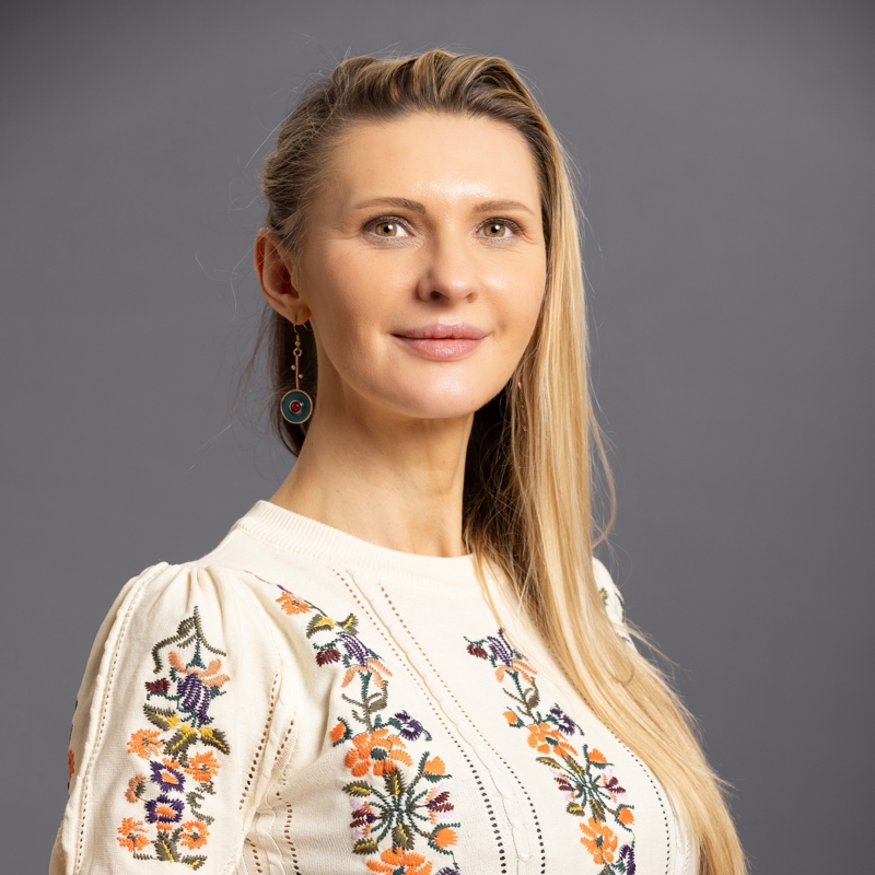 a person with long blonde hair wearing a white shirt with orange and purple flowers