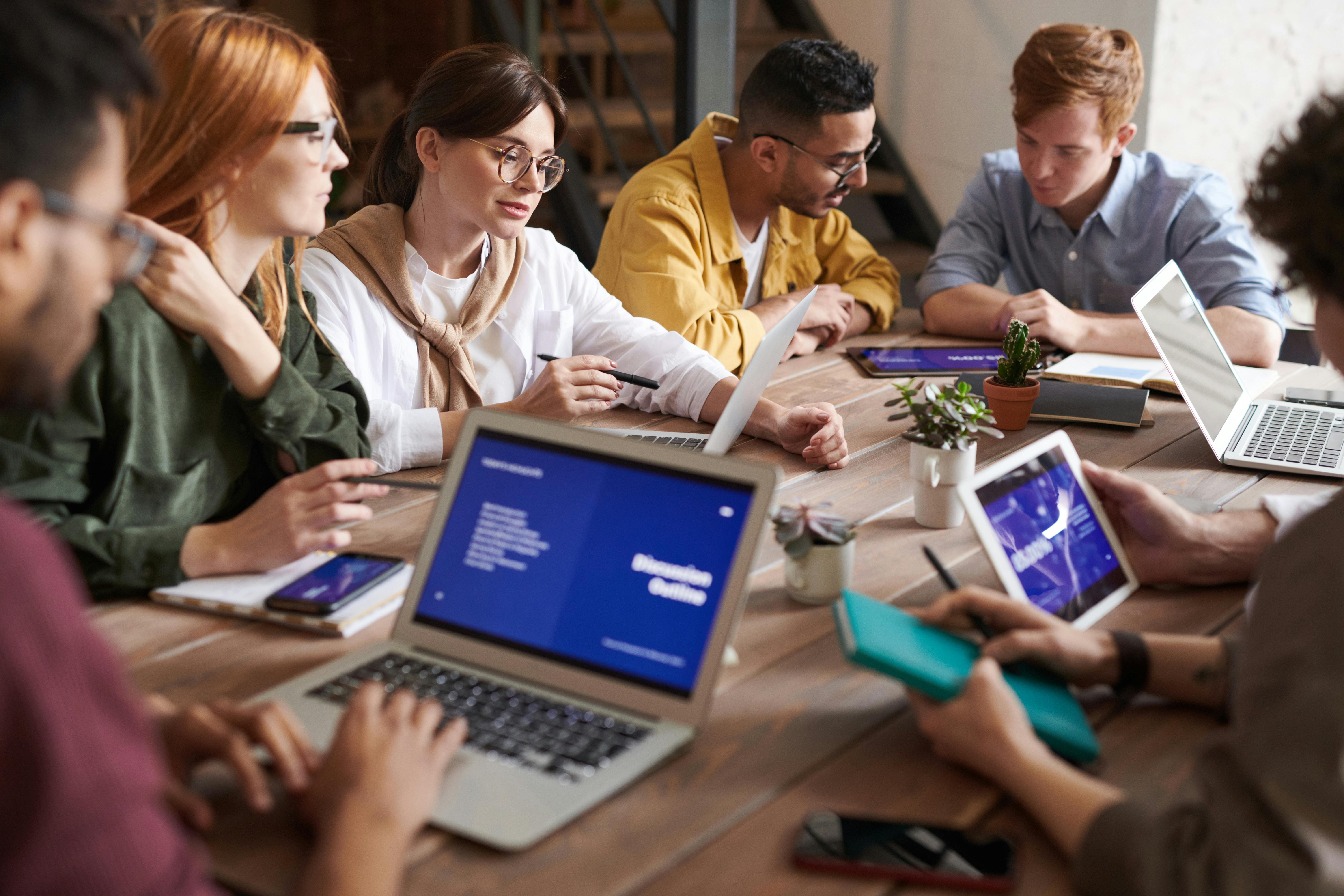 a group of people sitting around a table with laptops and tablets