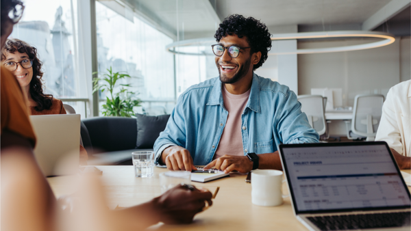 a person smiling at a table with a laptop