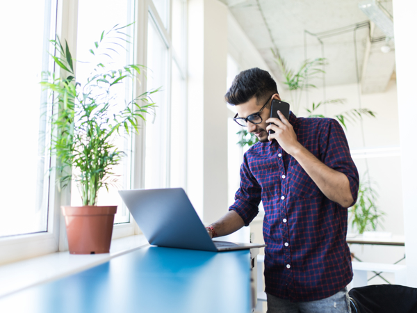 a person talking on a cell phone while using a laptop