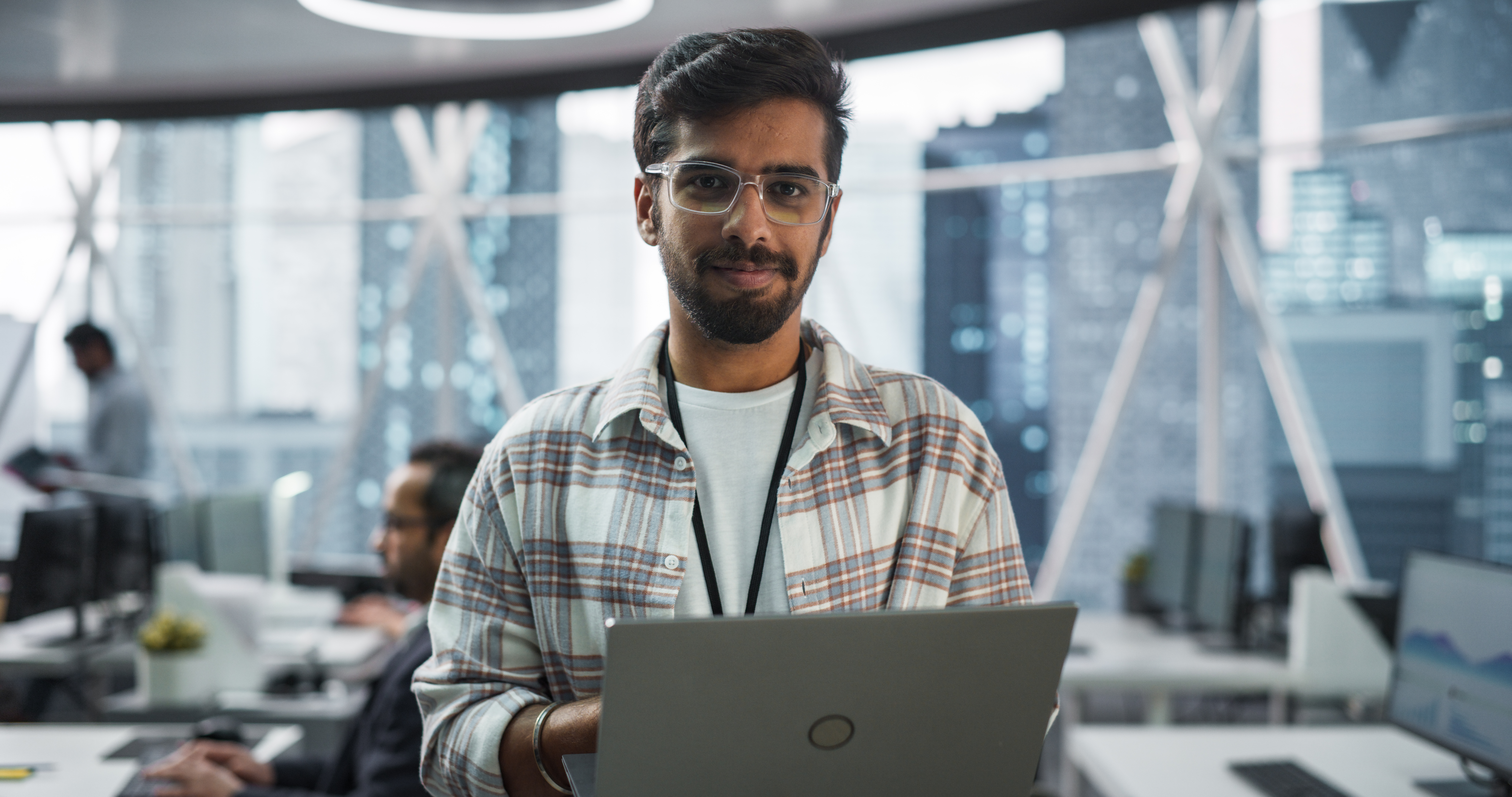 a person wearing glasses and a plaid shirt holding a laptop