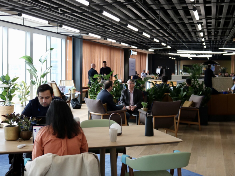 a group of people sitting at tables in a room with plants
